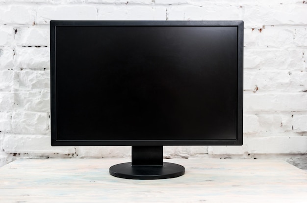 Computermonitor auf einem Tisch gegen weiße Ziegelsteinmauer leerer schwarzer Bildschirm