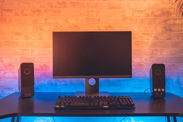 Computerspieler-Arbeitsplatz mit schwarzem Bildschirmmonitor mit Neonlicht und bunten Lichtern Gamer Rig