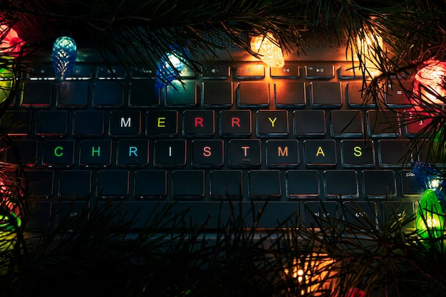 Computertastatur, Schlüssel mit Weihnachtsbaum, Nahaufnahme. Frohe Weihnachten die Aufschrift auf der Laptop-Tastatur im dunklen Licht nachts.