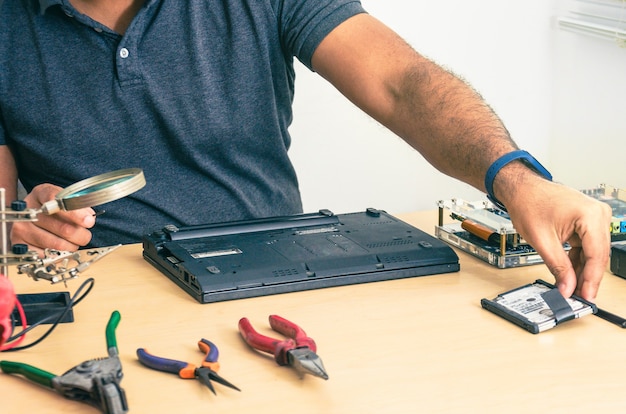 Computertechniker, der Laptop auf dem Schreibtisch repariert. Schwarzer Mann. Werkzeuge.