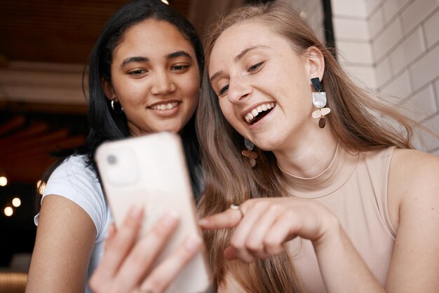 Jovens mulheres positivas com mulheres felizes assistem a vídeos engraçados  no smartphone e bebem coquetéis