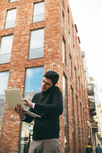 comunicação de mobilidade graças à tecnologia moderna. conexão constante com o cliente. homem de negócios trabalhando no laptop e falando ao telefone na rua. fundo urbano