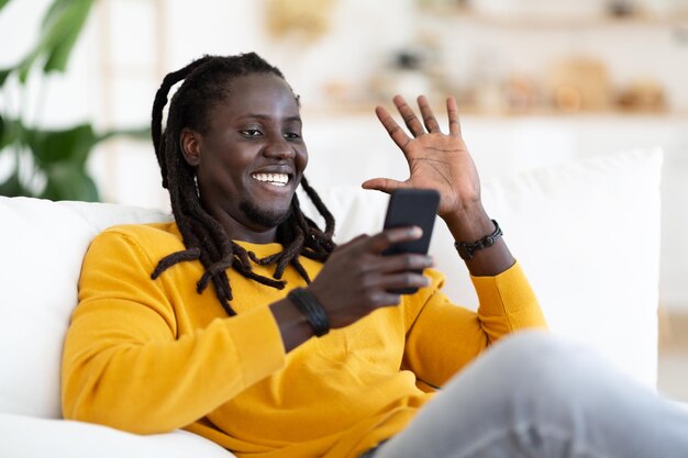 Comunicação distante sorridente negro fazendo videochamada via smartphone em casa