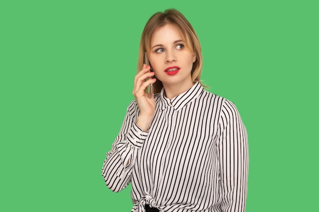 Comunicação móvel. Empresária preocupada com lábios vermelhos na blusa listrada de glamour ligando para o parceiro, falando no celular com séria expressão chateada. tiro de estúdio interno isolado em fundo verde