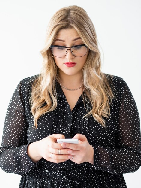 Comunicação móvel Pessoas de gadget Mídia social Corpo positivo Mulher obesa elegante e inteligente curiosa é óculos mandando mensagens de texto lendo mensagem no telefone isolado no branco