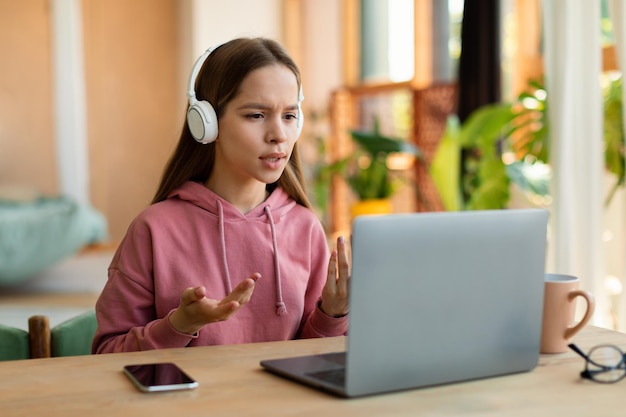 Comunicação online Adolescente falando na webcam do laptop usando fones de ouvido sem fio