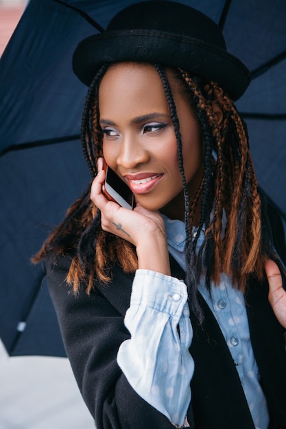 Comunicação social moderna. Mulher negra feliz. Clima temperamental, mulher afro-americana alegre com guarda-chuva em dia chuvoso, conceito de felicidade