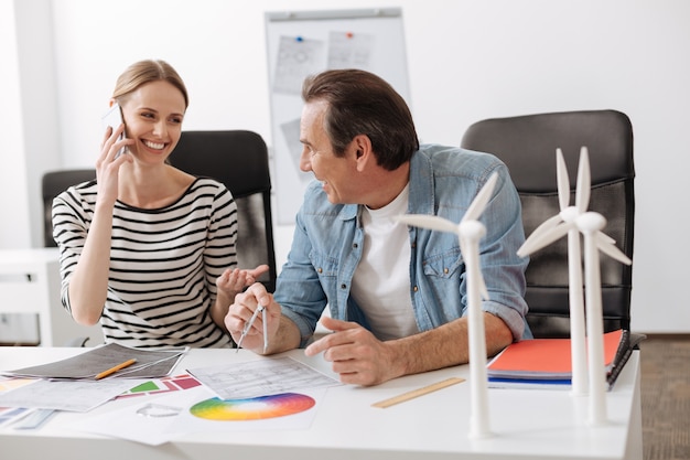 Comunicação viva. engenheiros profissionais alegres conversando e sentando à mesa enquanto trabalhavam no projeto de construção de turbinas eólicas