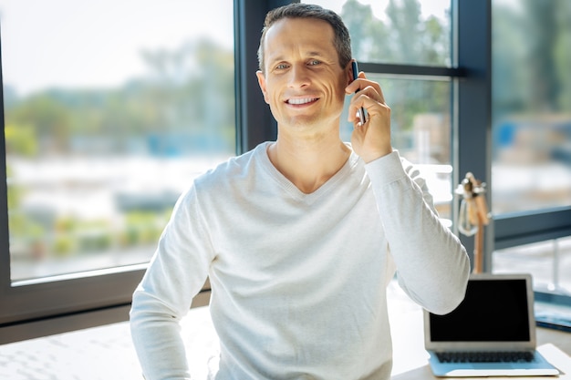 Comunicación agradable. Feliz agradable hombre encantado sonriendo y hablando por teléfono mientras tiene una comunicación agradable