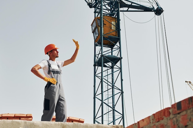 Comunicación con alguien El joven trabajador de la construcción uniformado está ocupado en el edificio sin terminar