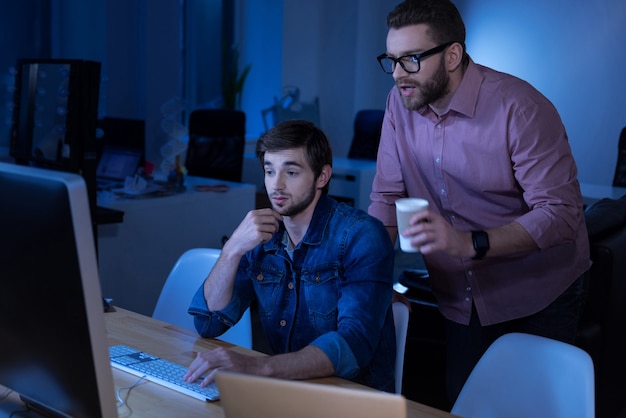 Comunicación con compañeros. Programadores masculinos guapos inteligentes que miran la pantalla de la computadora y discuten un proyecto mientras trabajan juntos