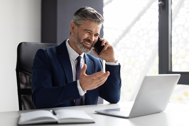 Comunicación corporativa apuesto hombre de negocios de mediana edad hablando por teléfono celular en la oficina