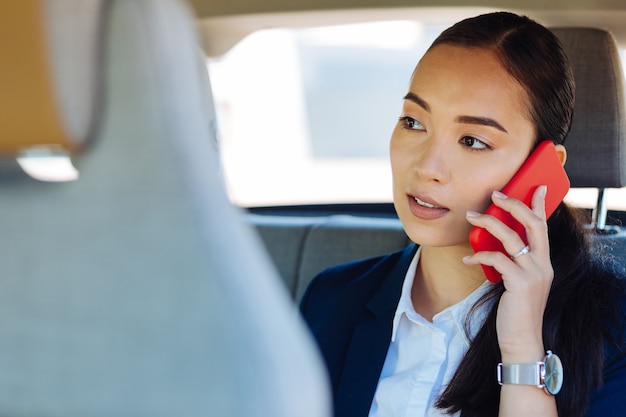 Comunicación a distancia. Mujer joven inteligente poniendo un teléfono en su oído mientras tiene una conversación