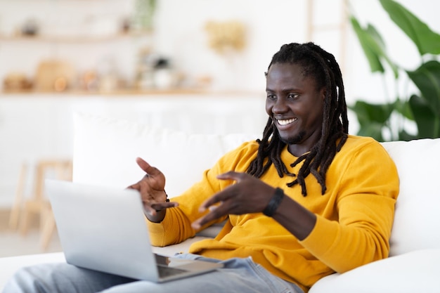 Comunicación distante Hombre negro sonriente haciendo videollamadas en la computadora portátil en casa