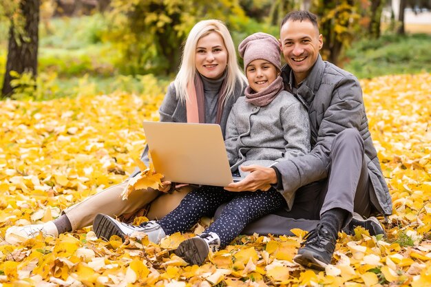 Comunicación en línea. Familia usando laptop y videollamadas, sentada en una manta de picnic en el jardín.