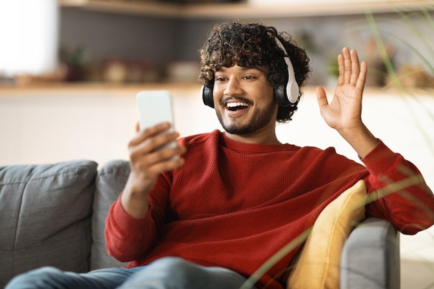 Comunicación en línea feliz chico indio haciendo videollamadas a través de un teléfono inteligente en casa