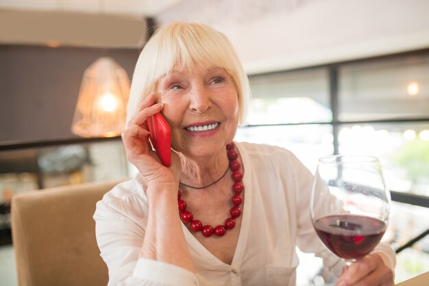 Comunicación. Mujer rubia tomando un poco de vino y hablando por teléfono