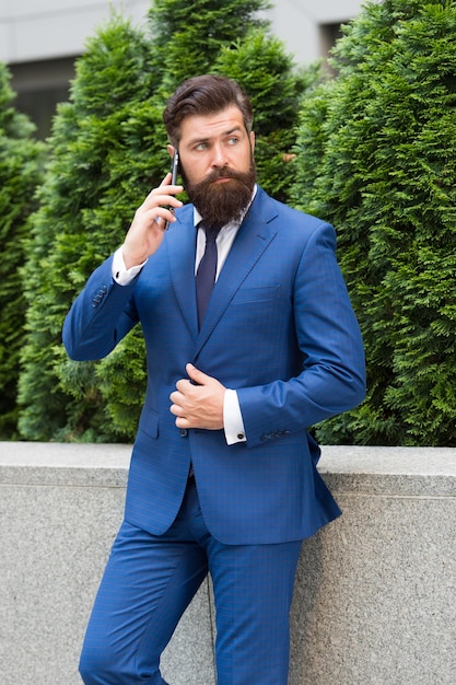 Comunicación de negocios Tecnología móvil Llamada de negocios Chico elegante usar esmoquin Manténgase conectado Empresario hablar teléfono móvil Hombre guapo con barba con teléfono celular al aire libre Estilo de vida móvil