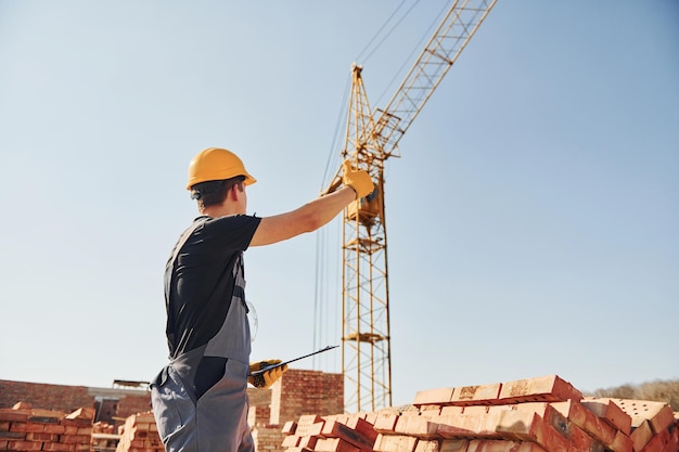 Comunicando-se com o cara do guindaste Trabalhador da construção civil em uniforme e equipamentos de segurança tem emprego na construção