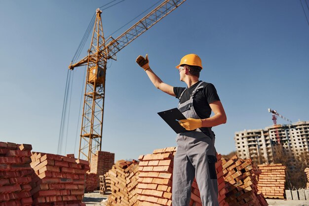 Comunicarse con el tipo de la grúa Trabajador de la construcción en uniforme y equipo de seguridad tiene trabajo en la construcción