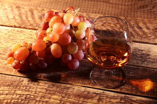 Coñac o brandy en un vaso y uvas frescas, naturaleza muerta en estilo rústico, fondo de madera vintage, enfoque selectivo.