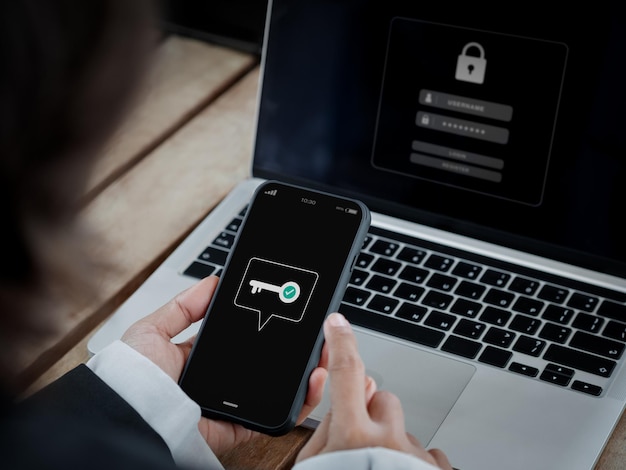 Conceito 2FA de autenticação de dois fatores Ícone de chave na tela do smartphone na mão perto do computador portátil para validar a página de senha Tecnologia de segurança cibernética de verificação de identidade