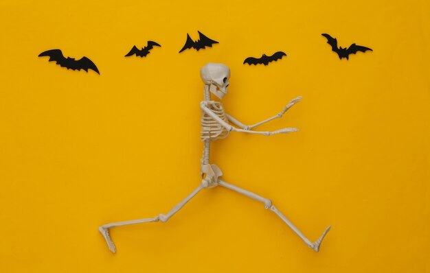 Conceito assustador de Halloween. Esqueleto foge amarelo com morcegos voadores