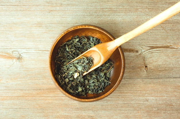 Conceito chinês, folhas de chá verde japonês seco na colher de bambu e tigela redonda fechem na vista superior de madeira natural. espaço de cópia de texto