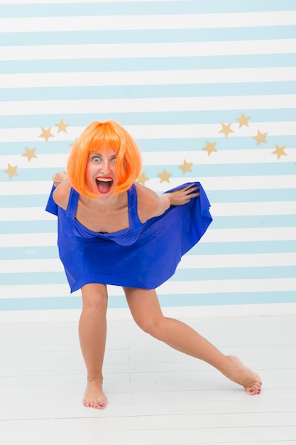 Conceito cômico e bem-humorado Mulher humor brincalhão se divertindo Diversão e entretenimento Menina peruca posando fundo listrado de estúdio Crie seu próprio humor Senhora peruca vermelha ou gengibre posando em vestido azul