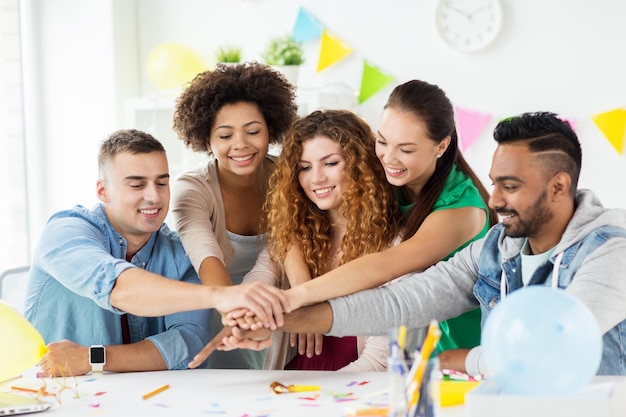 Conceito corporativo, de celebração e feriados - equipe feliz com confete divertindo-se na festa de aniversário no escritório de mãos dadas