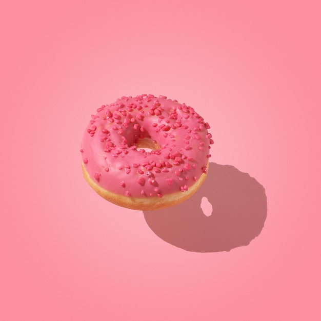 Conceito criativo de comida doce. um donut rosa flutuando acima de um fundo rosa.