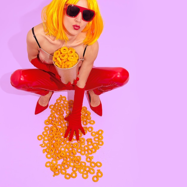 Conceito criativo de fast food Arte minimalista Garota em calças de couro vermelho e sapatos com anéis de queijo de milho Estilo de moda discoteca de festa em casa