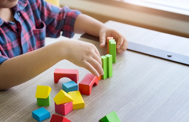 Foto conceito criativo; o menino joga blocos de madeira coloridos em casa.
