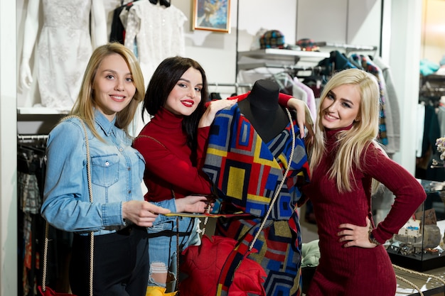 Conceito da compra, da forma e da amizade - três amigos de sorriso que tentam em alguma roupa no shopping.