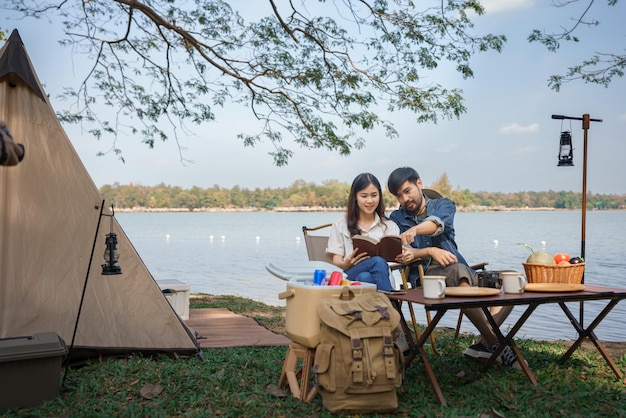 Conceito de acampamento Lazer de mochileiros de casal jovem com livro de leitura juntos enquanto acampava perto do lago