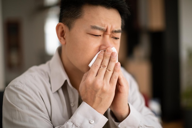 Conceito de alergia à gripe fria homem asiático de meia-idade doente espirrando em guardanapo doente sentindo-se mal