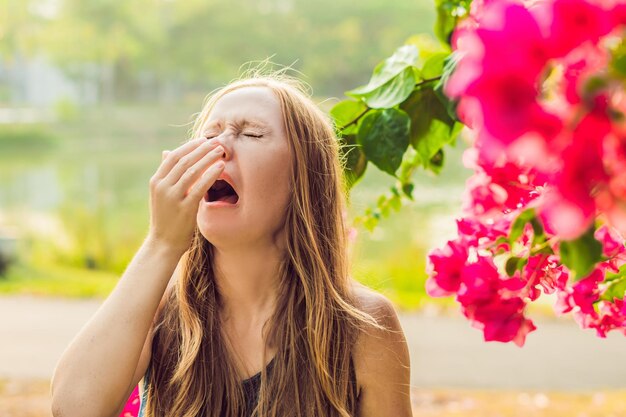 Conceito de alergia ao pólen. Mulher jovem vai espirrar. Árvores floridas no fundo