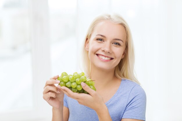 Conceito de alimentação, comida, frutas, dieta e pessoas saudáveis - mulher feliz comendo uvas em casa