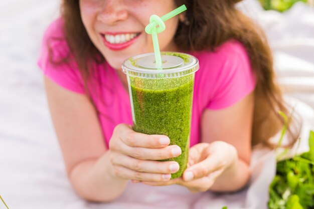 Conceito de alimentação, verão e pessoas saudáveis - jovem se divertindo no parque e bebendo smoothies verdes em um piquenique de perto