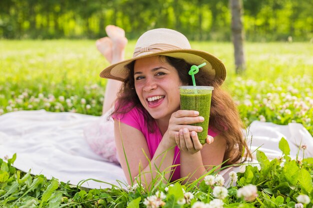 Conceito de alimentação, verão e pessoas saudáveis - uma jovem se diverte no parque e bebe smoothies verdes em um piquenique