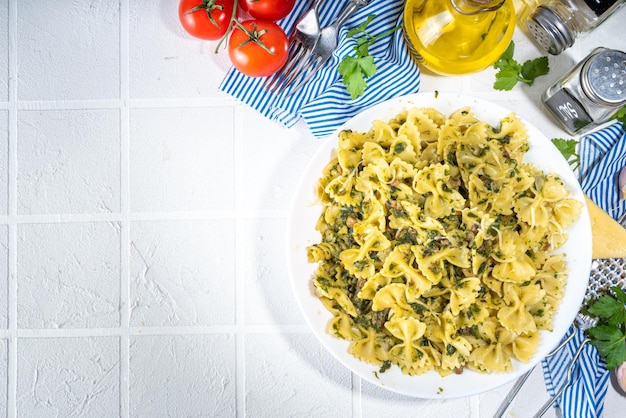 Conceito de almoço mediterrâneo italiano Macarrão Farfalle com legumes de cogumelos espinafre e molho cremoso Em uma mesa de azulejos brancos com especiarias para o espaço de cópia do jantar