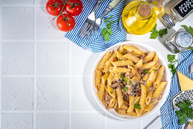 Conceito de almoço mediterrâneo italiano Macarrão penne com molho cremoso de cogumelos carbonara Em uma mesa de azulejos brancos com especiarias para o espaço de cópia do jantar