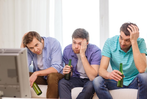 conceito de amizade, esportes e entretenimento - amigos do sexo masculino tristes com cerveja assistindo esportes na tv em casa