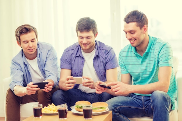 Foto conceito de amizade, tecnologia, comida e lazer - amigos sorridentes tirando foto de comida com câmera de smartphone em casa