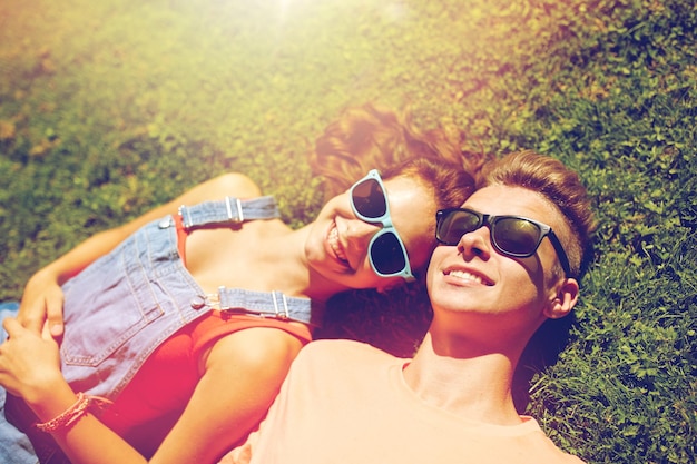 Foto conceito de amor e pessoas - casal adolescente feliz em óculos de sol, deitado na grama no verão