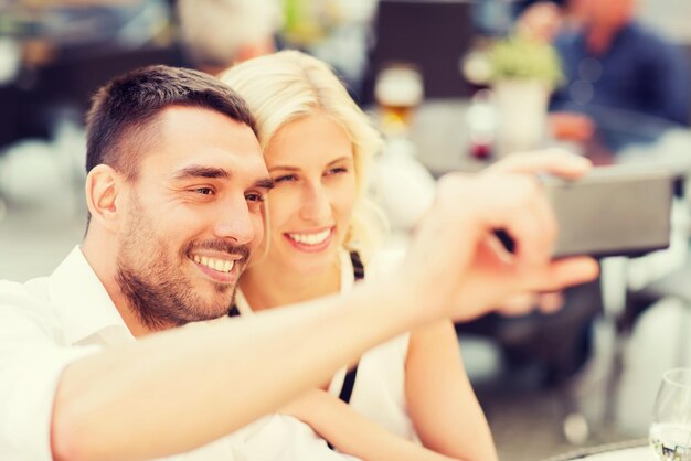 conceito de amor, encontro, tecnologia, pessoas e relações - casal feliz sorridente tomando selfie com smartphone no café de rua da cidade