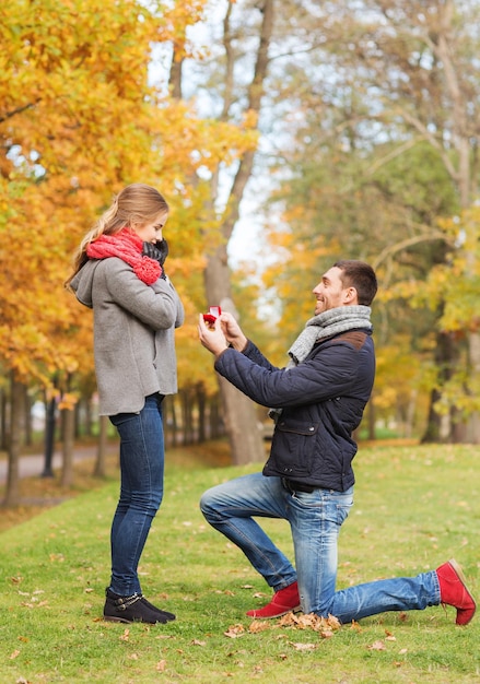 Conceito de amor, família, outono e pessoas - casal sorridente com anel de noivado em pequena caixa de presente vermelha ao ar livre