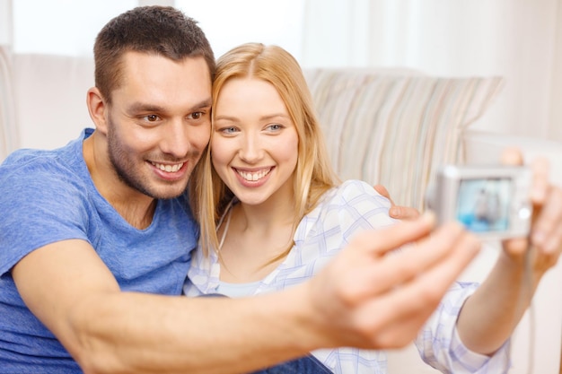 conceito de amor, família, tecnologia e felicidade - casal sorridente tirando foto de autorretrato com câmera digital em casa