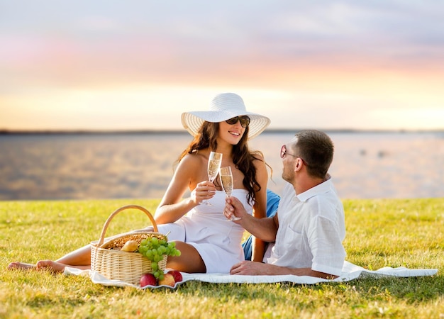 Conceito de amor, namoro, pessoas e feriados - casal feliz bebendo champanhe no piquenique sobre o fundo do pôr do sol à beira-mar