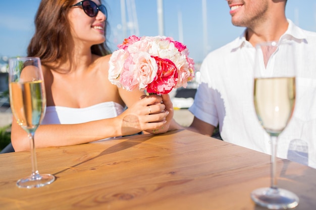 Conceito de amor, namoro, pessoas e feriados - casal sorridente com um monte de flores e taças de champanhe e olhando um para o outro no café